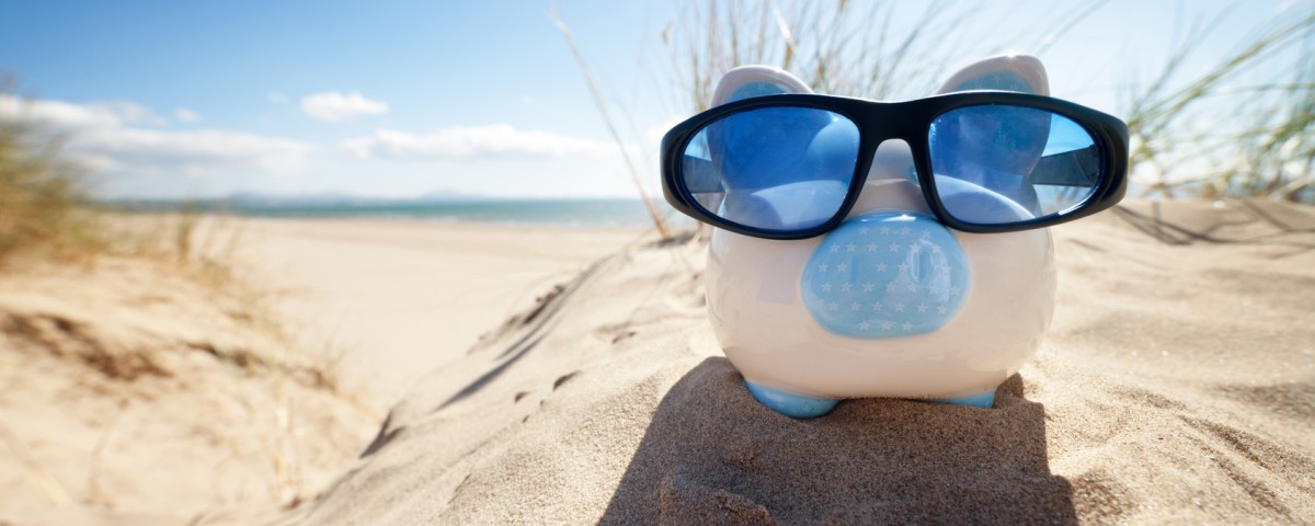 Holiday savings piggy bank on a beach vacation with sunglasses